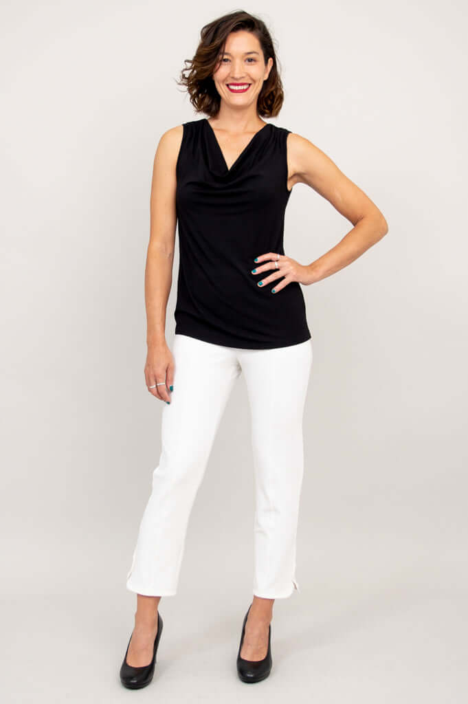 Full body front view of a woman in a black sleeveless cowl neck top and white pants