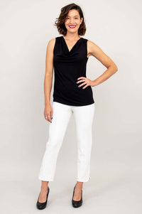 Full body front view of a woman in a black sleeveless cowl neck top and white pants