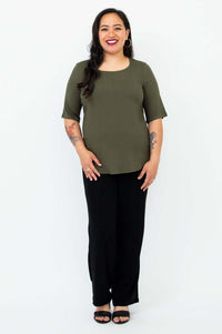 Full body front view of a woman dressed in an olive green blouse and black pants