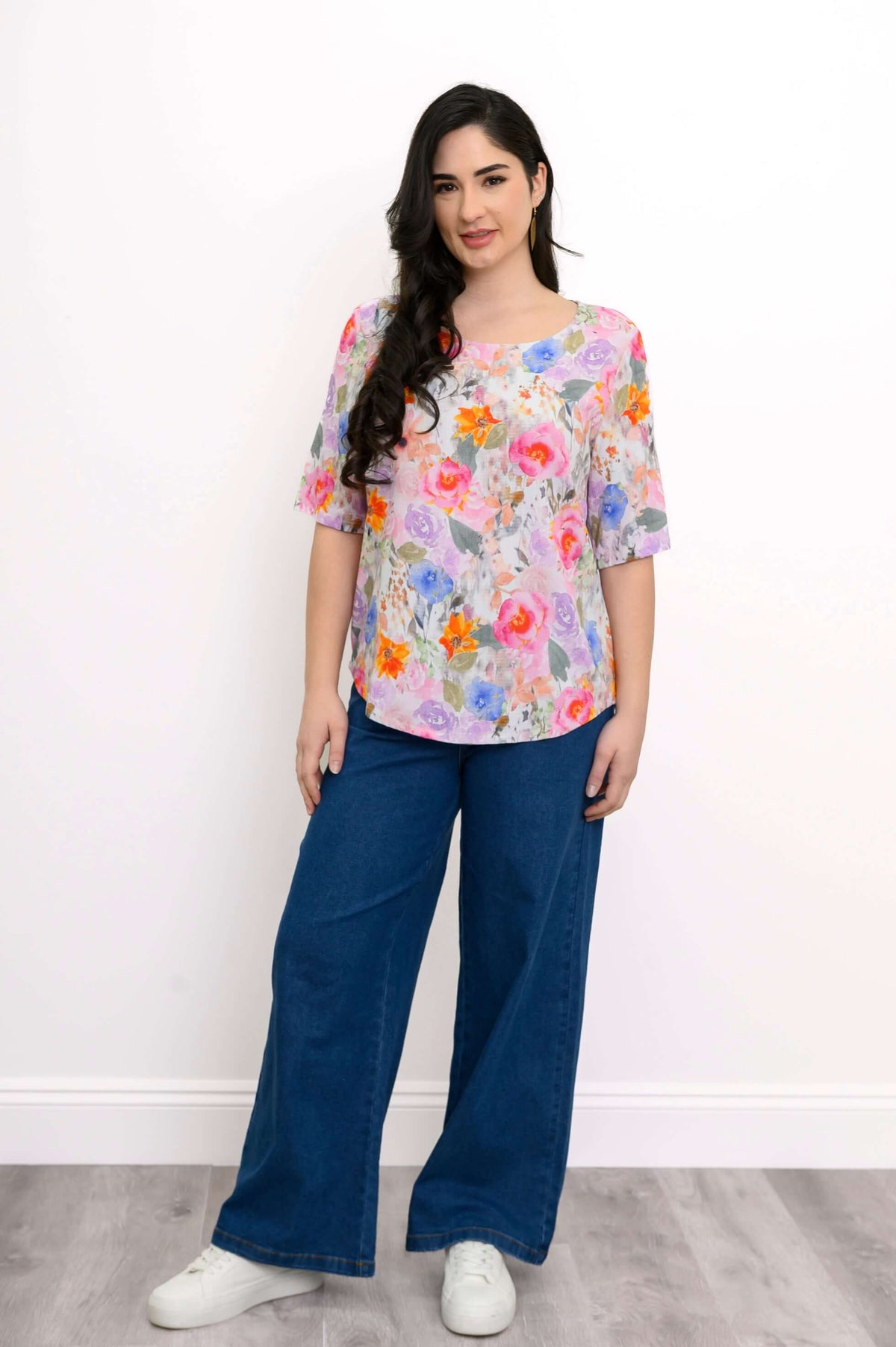 Full body front view of model in Liza floral blouse and blue pants with white sneakers