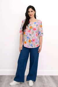 Full body front view of model in Liza floral blouse and blue pants with white sneakers