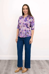 Woman standing in purple floral blouse and blue jeans, full body front view