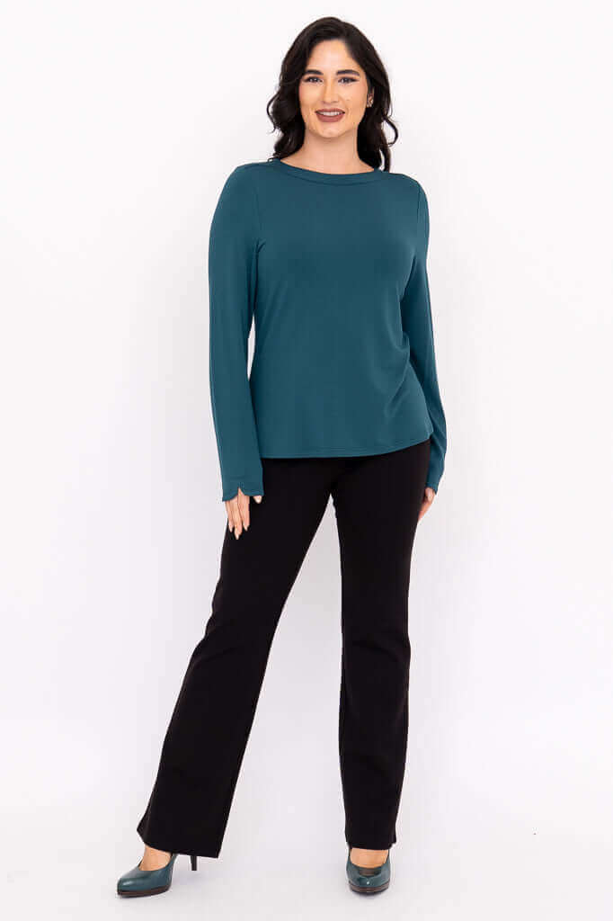 Full body front view of a woman in a teal boat neck top with black pants and teal shoes