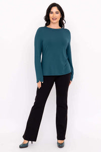 Full body front view of a woman in a teal boat neck top with black pants and teal shoes