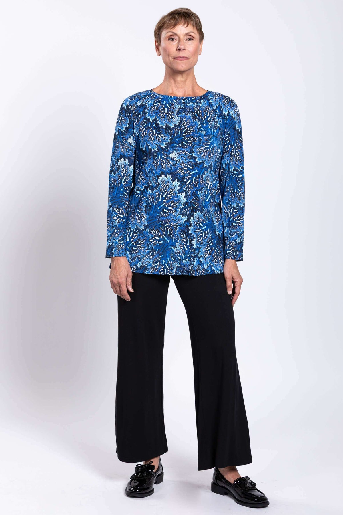 Full body front view of woman in blue botanical print top and black pants