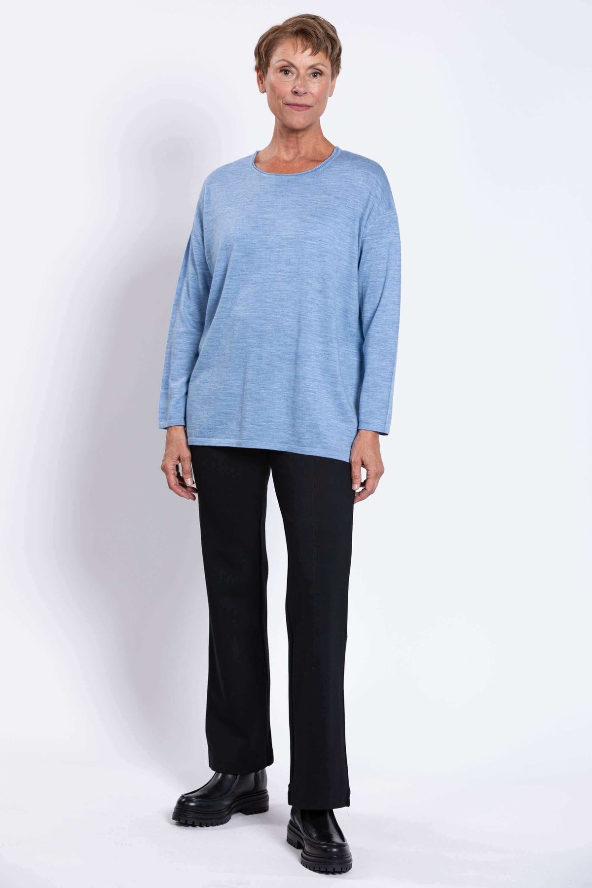 Full front view of a woman in a light blue merino wool sweater and black pants with boots