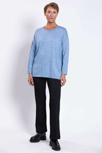 Full front view of a woman in a light blue merino wool sweater and black pants with boots