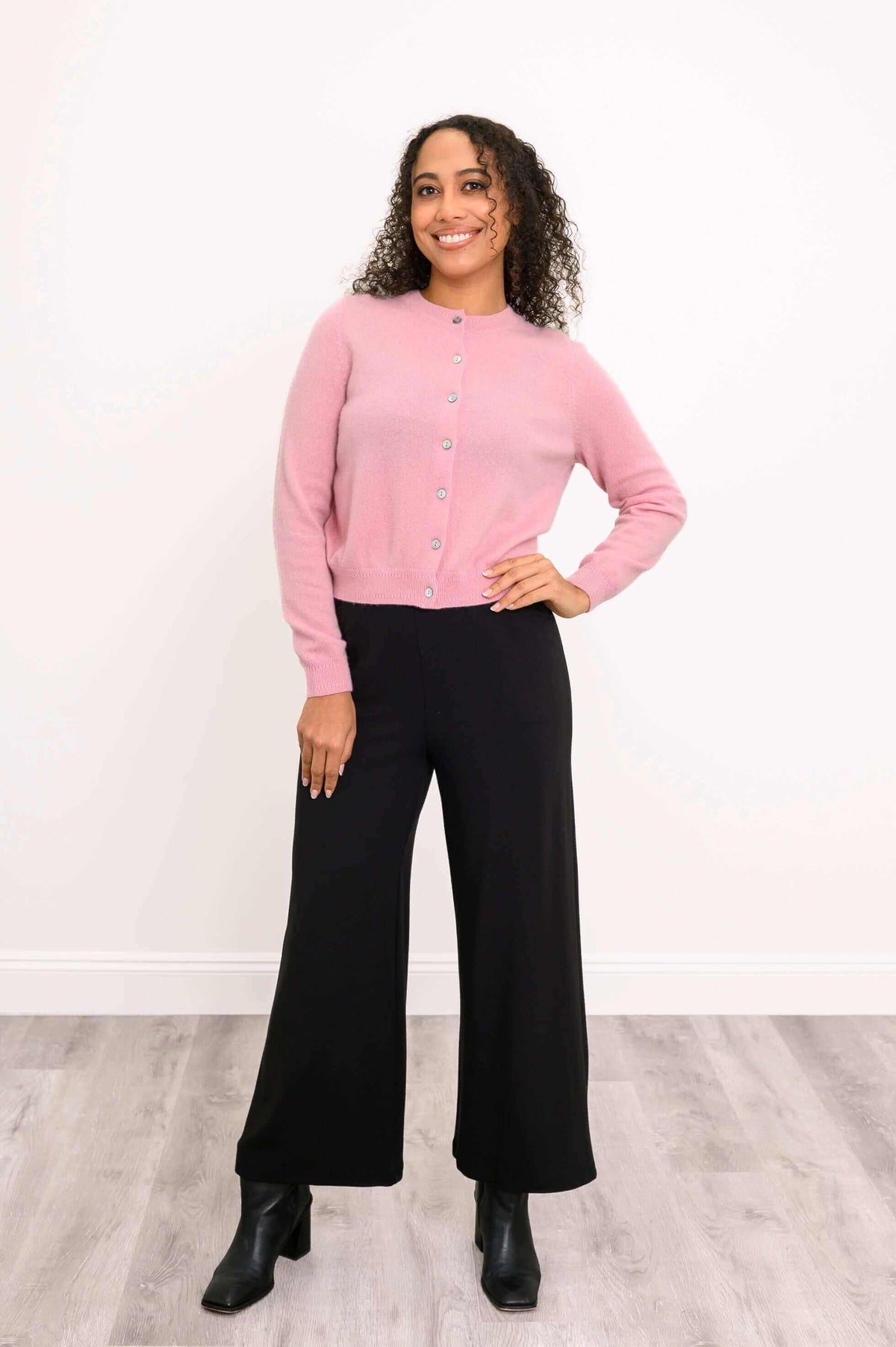 Full body front view of woman modeling pink cardigan with black pants and boots