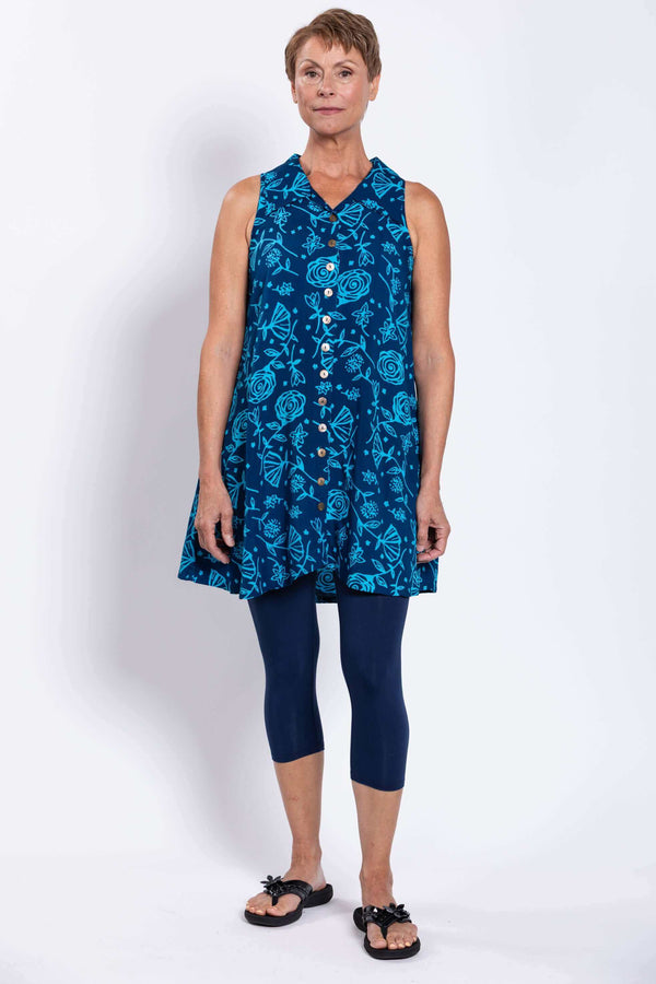 Full body front view of woman in sleeveless blue tank dress with floral print, button-up front, and navy leggings