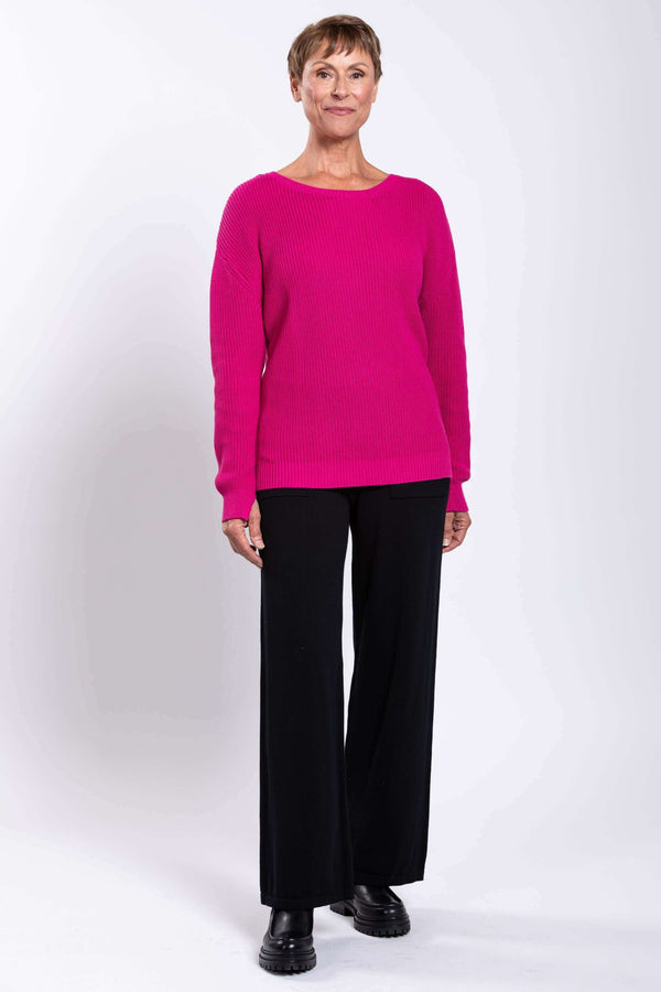 Full body front view of a woman modeling a fuchsia sweater with black pants