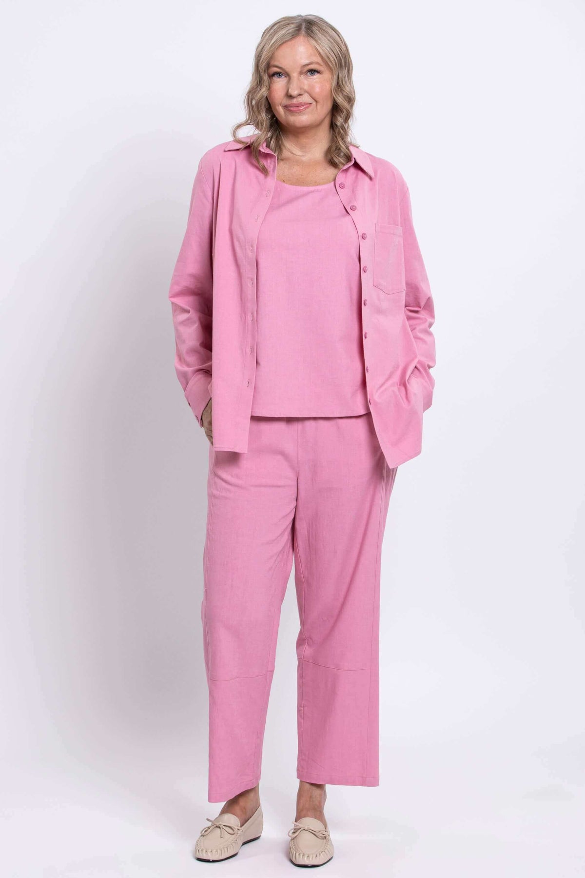 Woman dressed in a pink shirt and pants set, full body front view with beige moccasins