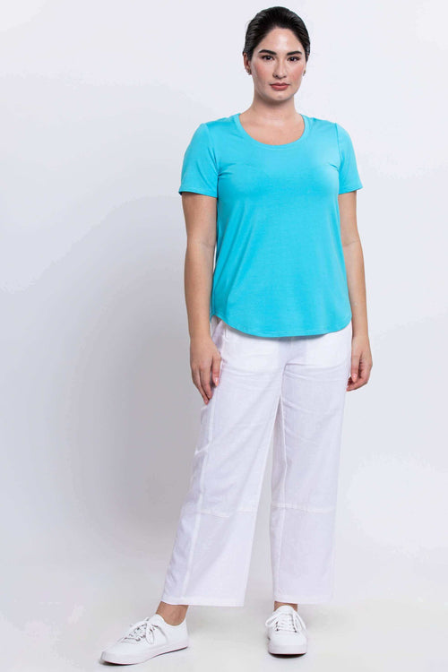 Woman modeling turquoise tee and white pants, full body front view