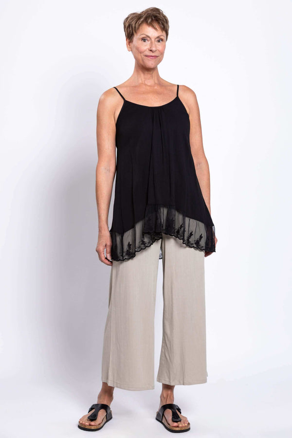Full body view of a woman in a black tank top with lace hem and beige pants