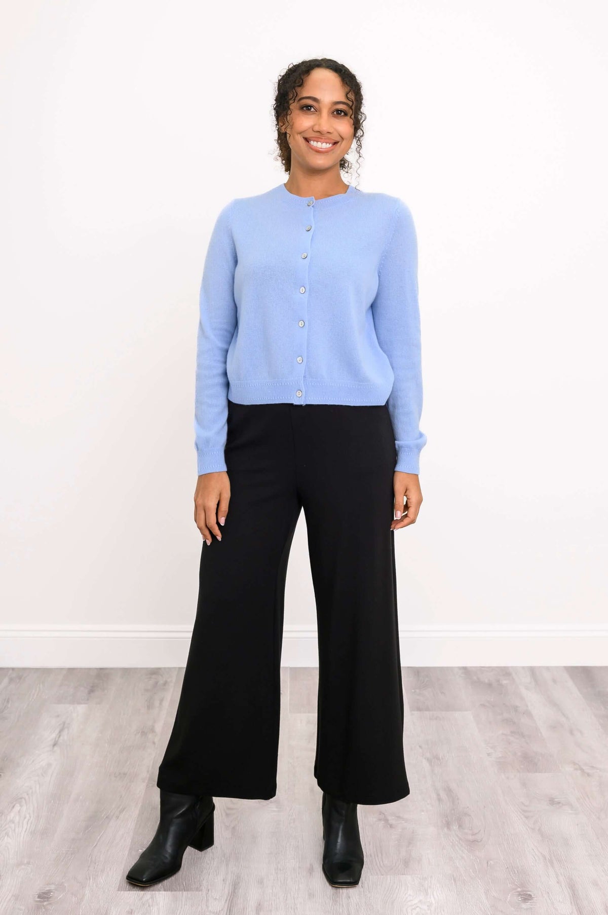 Full body view of a woman in a light blue cashmere cardigan and black wide-leg pants
