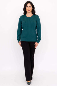 Full body view of woman in teal cable knit sweater and black pants