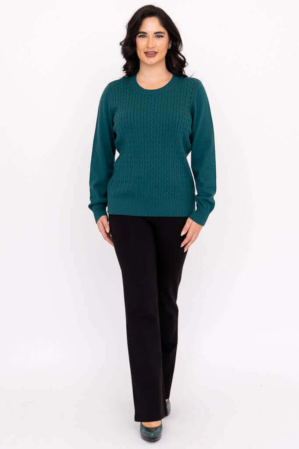 Full body view of woman in teal cable knit sweater and black pants