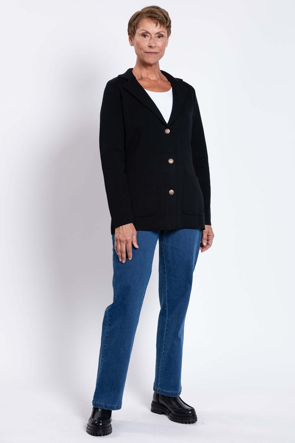 Full body view of a woman modeling the black Margaret Jacket, styled with blue jeans and boots