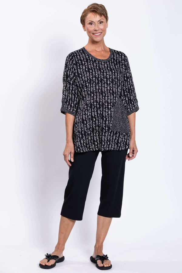 Full body view of a model in the black and white Palace Blouse paired with black capri pants