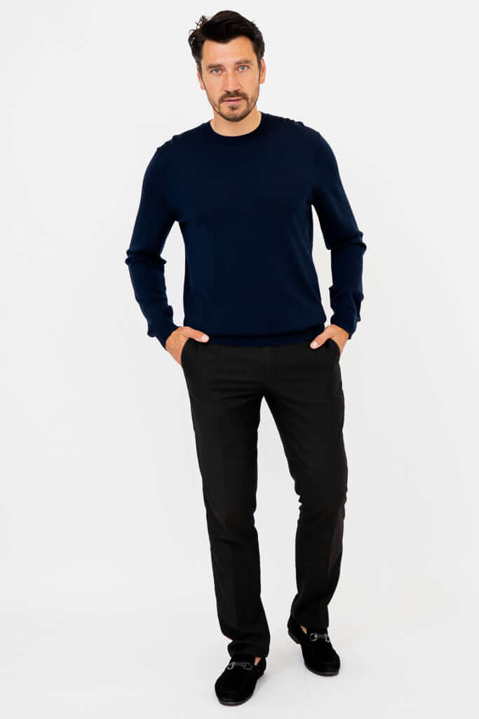Full body view of man in navy sweater and black pants, standing against white background
