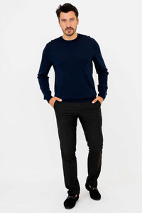 Full body view of man in navy sweater and black pants, standing against white background
