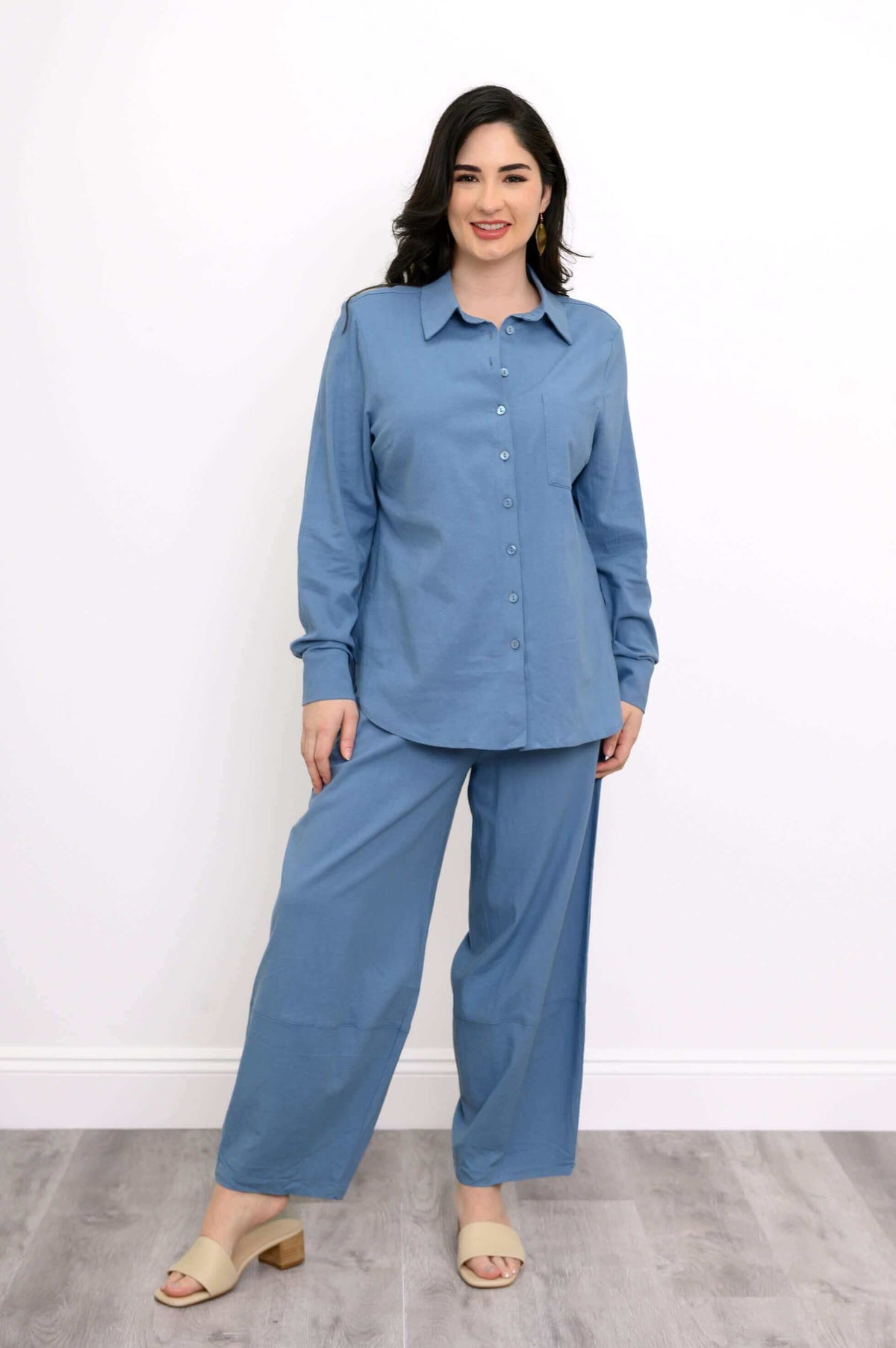 Full view of a woman in a blue button-up shirt and wide-leg pants on a wood floor
