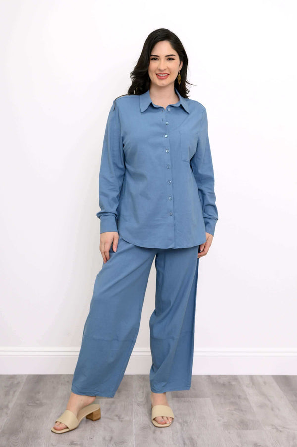 Full view of a woman in a blue button-up shirt and wide-leg pants on a wood floor