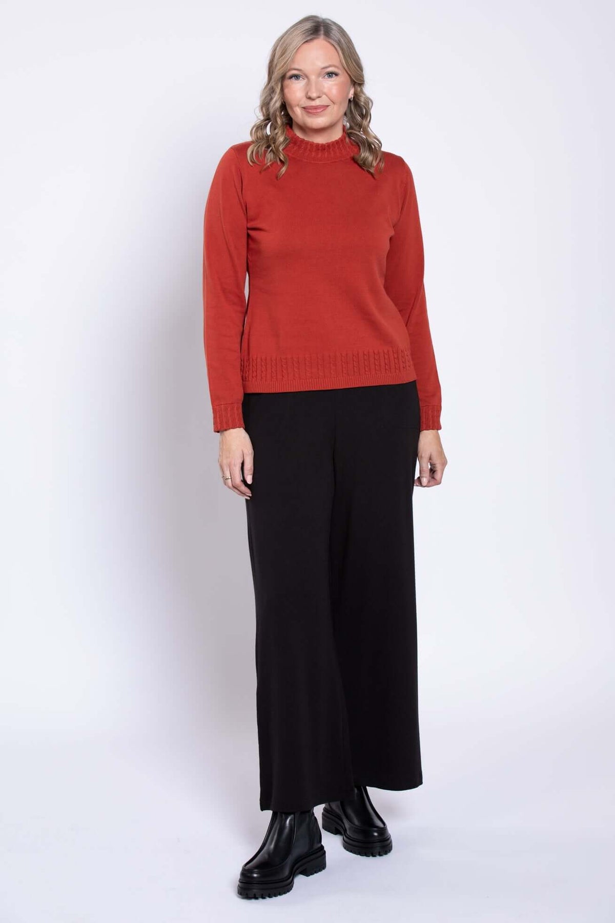 Full body view of a woman in a rust red mock neck sweater and wide leg black pants