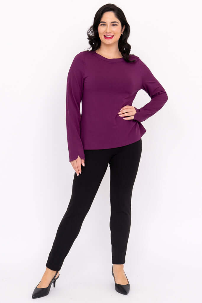 Woman in a purple boat neck top and black pants, full body pose