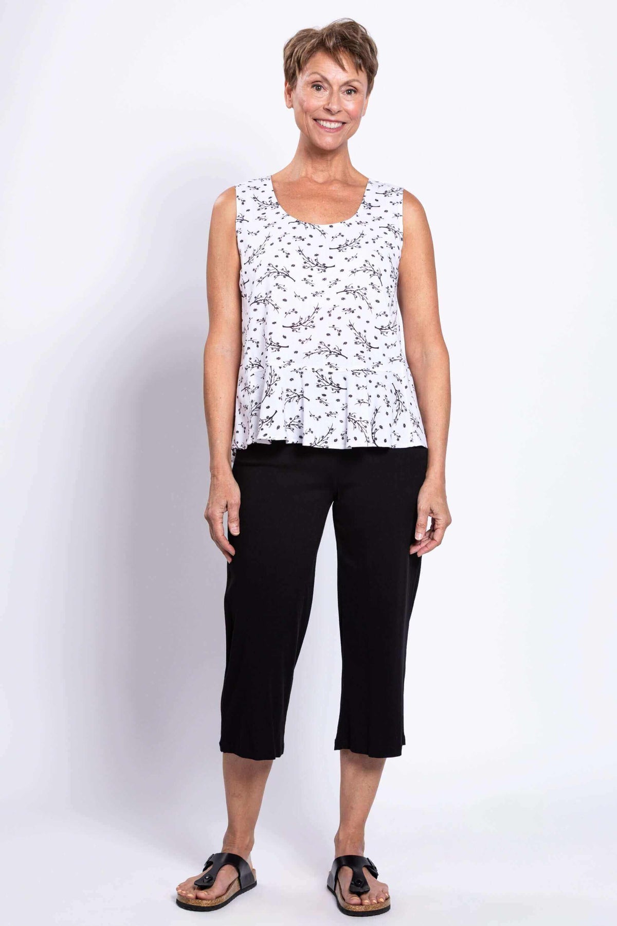 Full body view of woman in white floral peplum tank and black pants