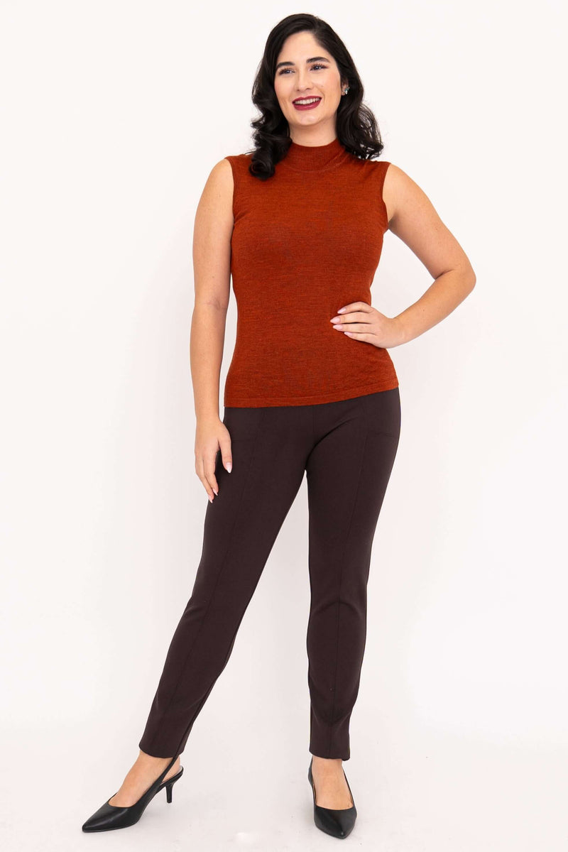 Full body view of a woman wearing a rust-colored sleeveless mock neck sweater with brown pants and black heels