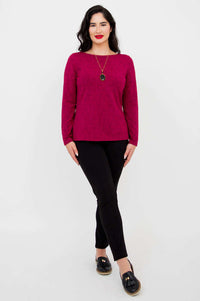 Full body view of woman in berry long sleeve top and black pants, standing on white background