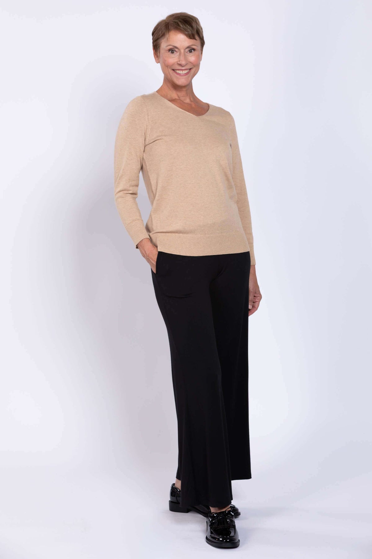 Full body view of woman in beige V-neck sweater and black wide-leg pants