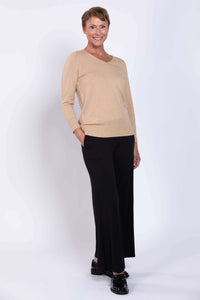 Full body view of woman in beige V-neck sweater and black wide-leg pants