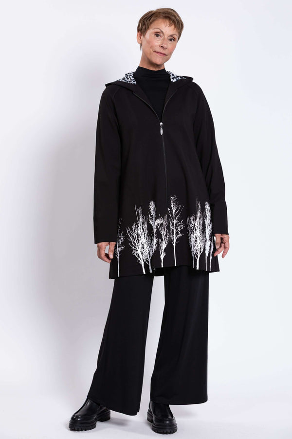 Full body view of model in black coat with hood and white tree print at the hem