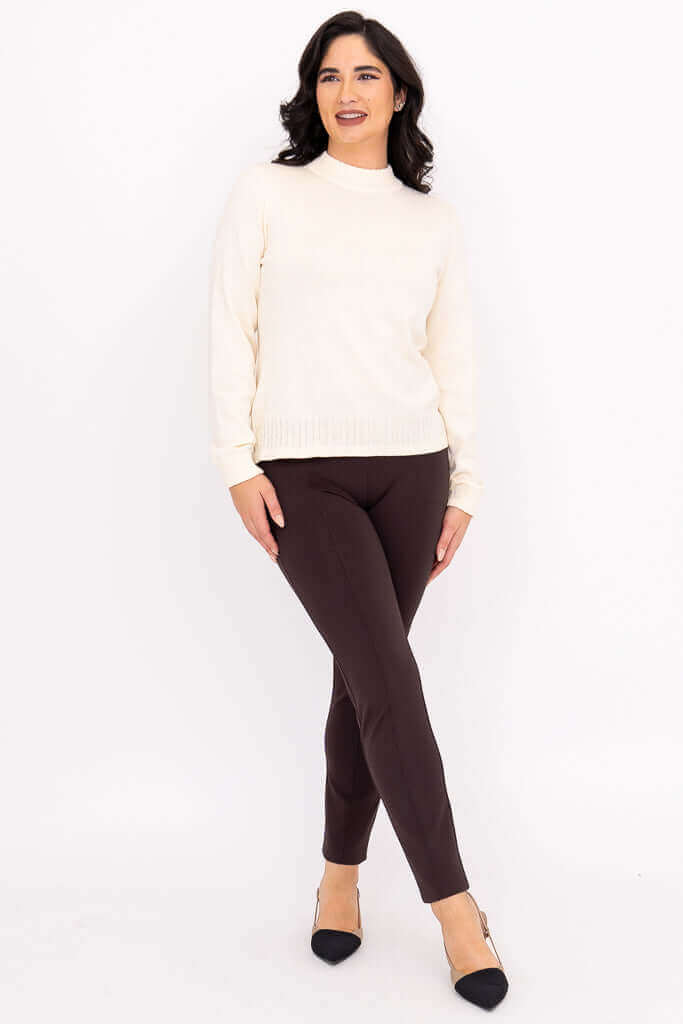 Full body view of woman wearing ivory sweater and brown slim-fit pants