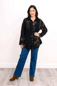 Full body view of woman in black smocked floral tunic shirt, blue jeans, and brown boots