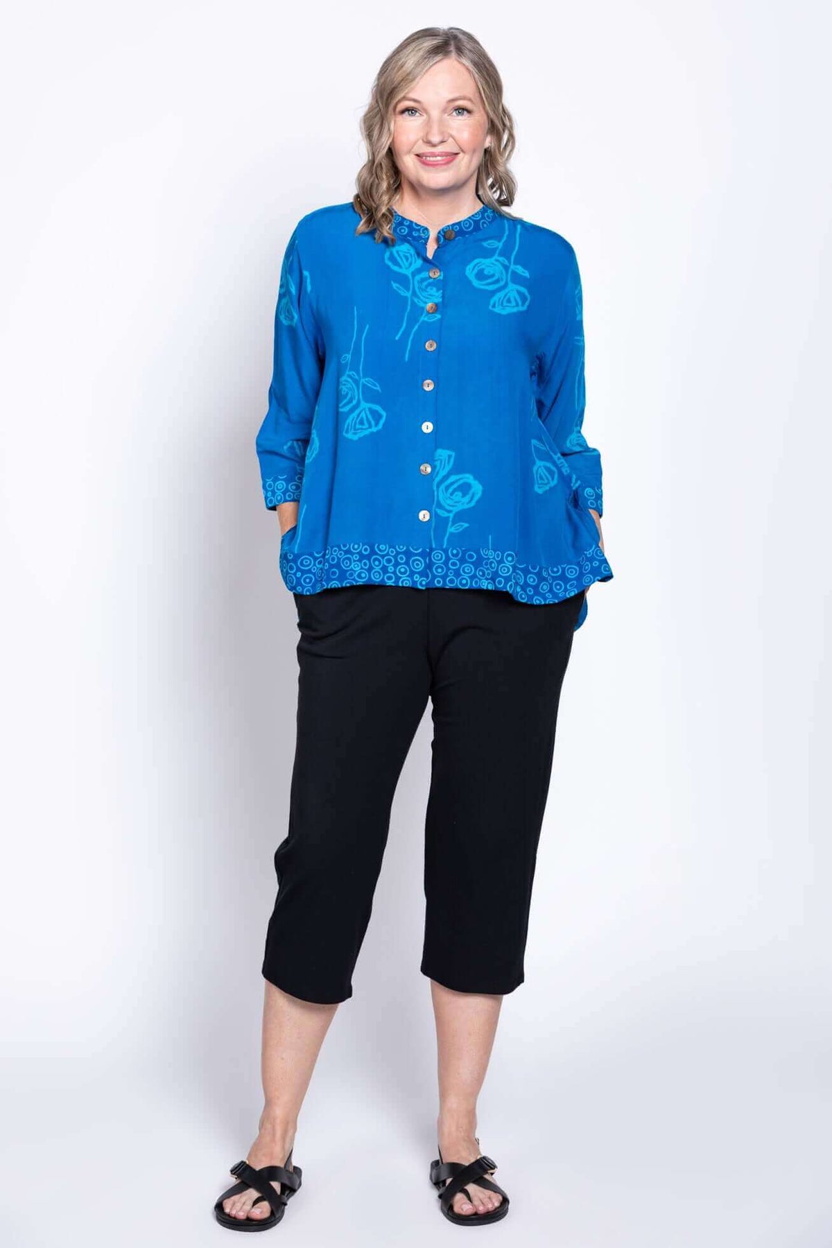 Full body view of a woman in a blue floral blouse with black cropped pants and sandals