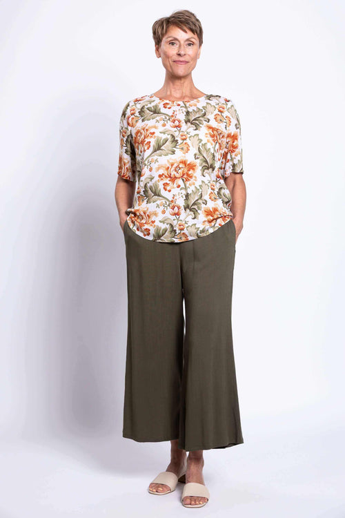 Full body view of a woman in a floral blouse and olive wide leg pants
