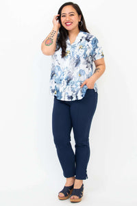 Full body view of woman in a blue floral shirt and navy capri pants smiling