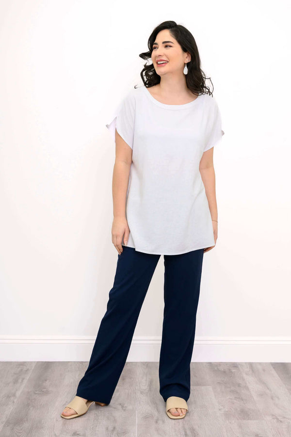 Full body view of woman in white tee and navy pants, standing and smiling