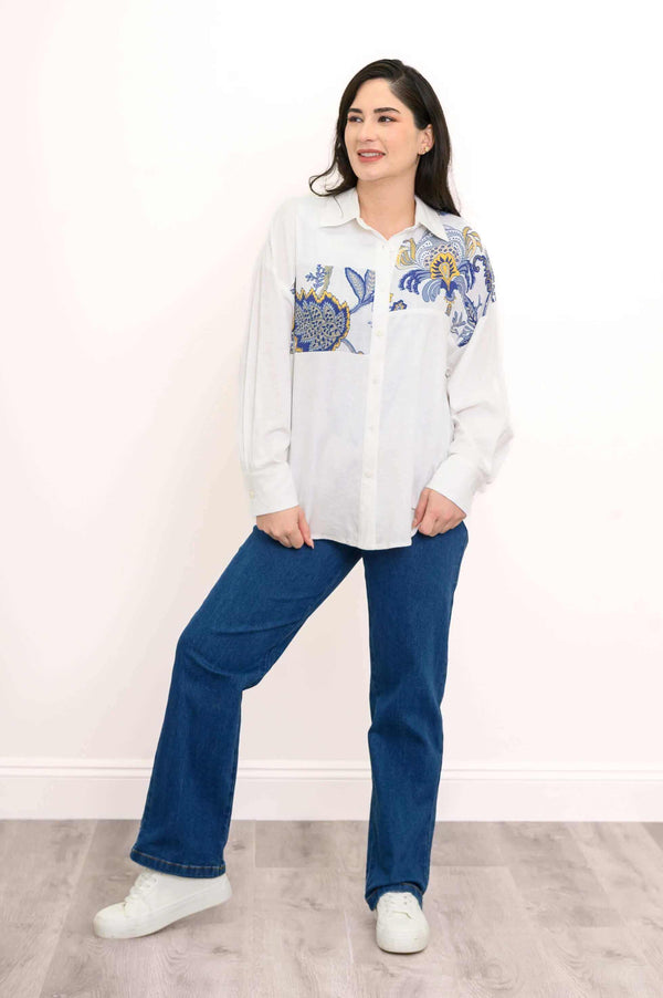 Full body view of woman in white blouse with blue and gold floral design, styled with jeans