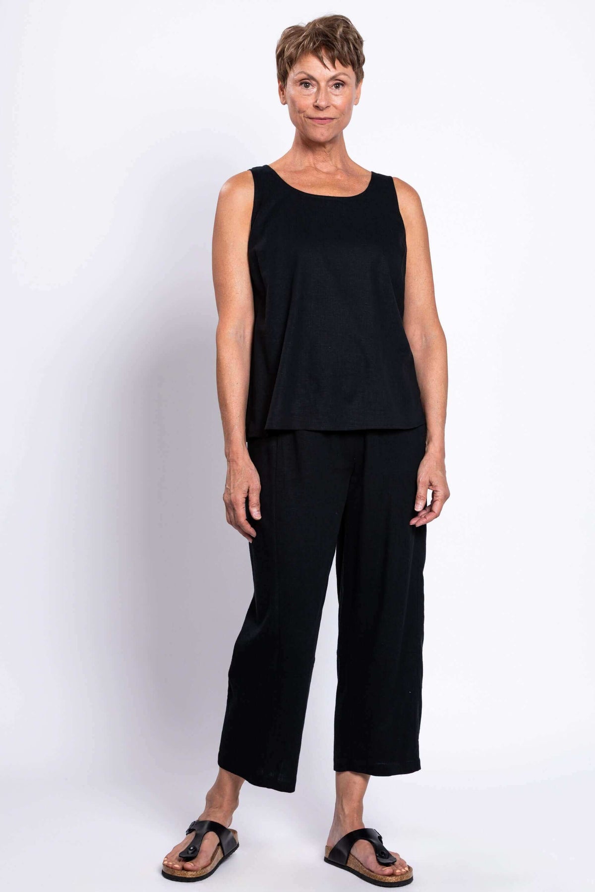 Full body view of woman in black tank top and pants, facing forward
