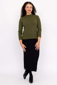 Full view of woman in olive green sweater and black skirt, standing against white background