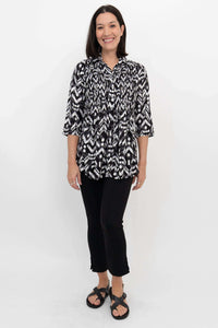 Full front view of model in patterned black and white pleated blouse and black pants