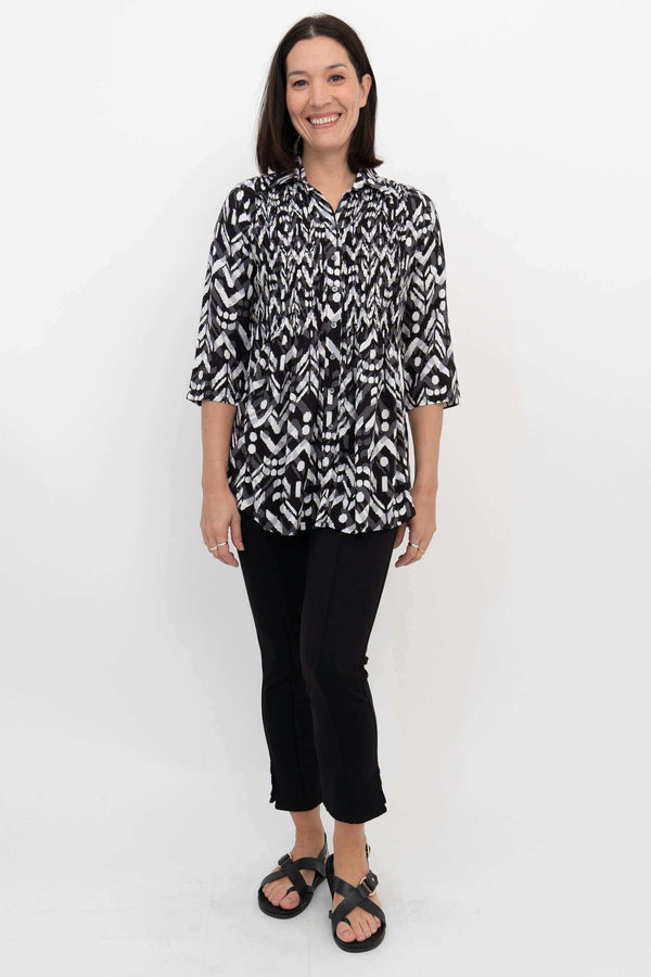Full front view of model in patterned black and white pleated blouse and black pants
