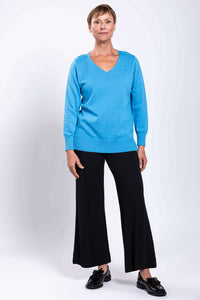 Full front view of woman in blue V-neck cotton sweater and black pants