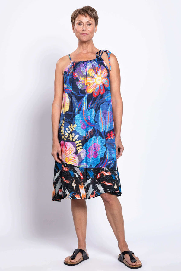 Full body front view of a woman in a vibrant sleeveless floral summer dress with one tie strap