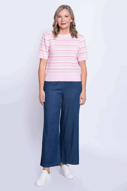 Full body front view of woman in pink striped dot sweater and blue wide-leg pants