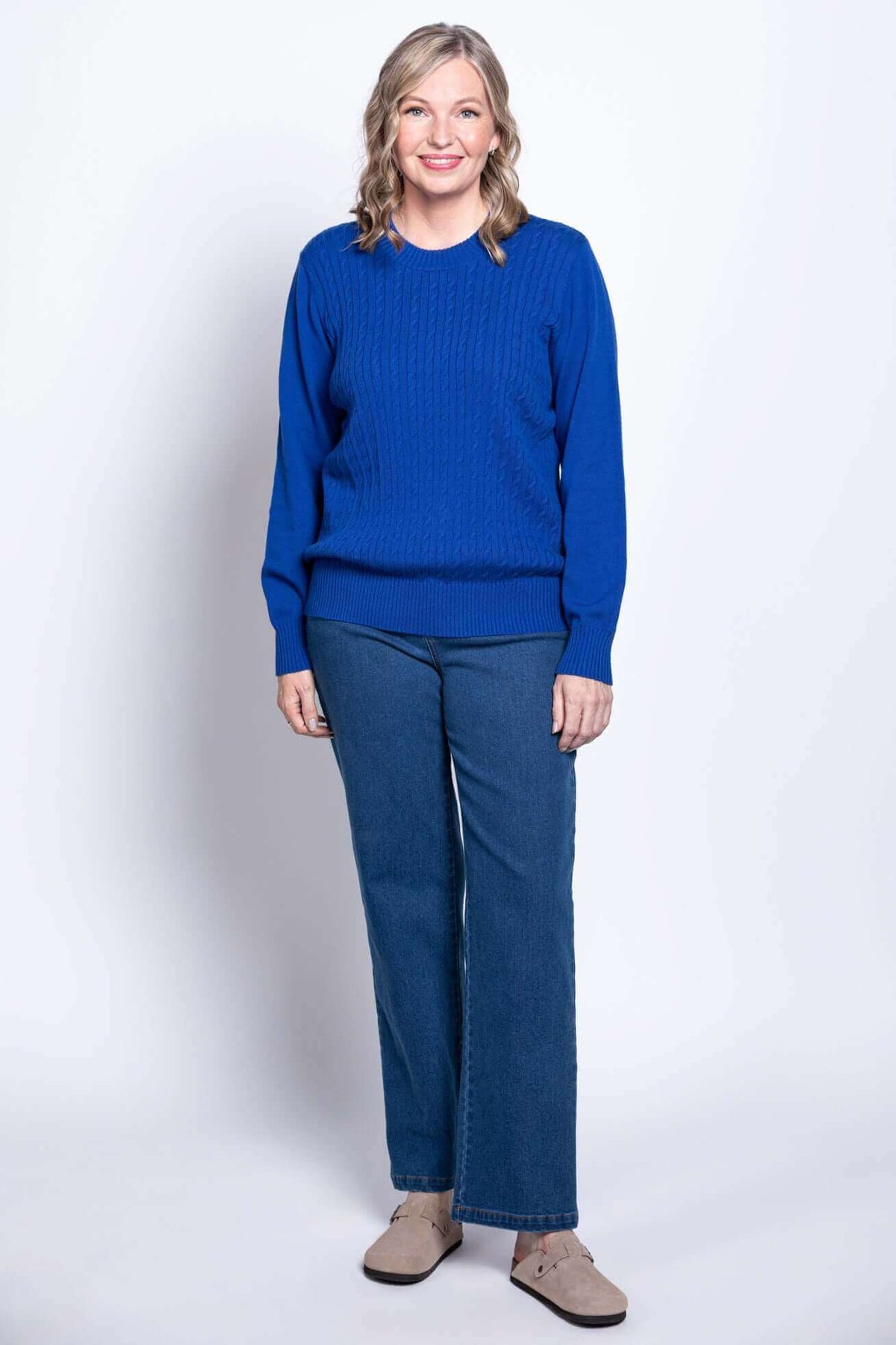 Full length view of woman in blue cable knit sweater and blue jeans, facing forward