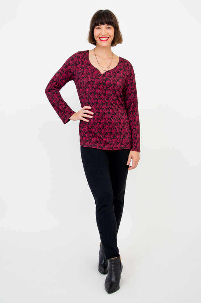 Full length image of a woman in magenta and black patterned long sleeve top and black pants